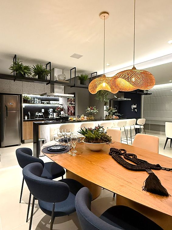 Espaço gourmet de área comum com mesa de madeira, cadeiras azul-marinho e pendentes de fibra.